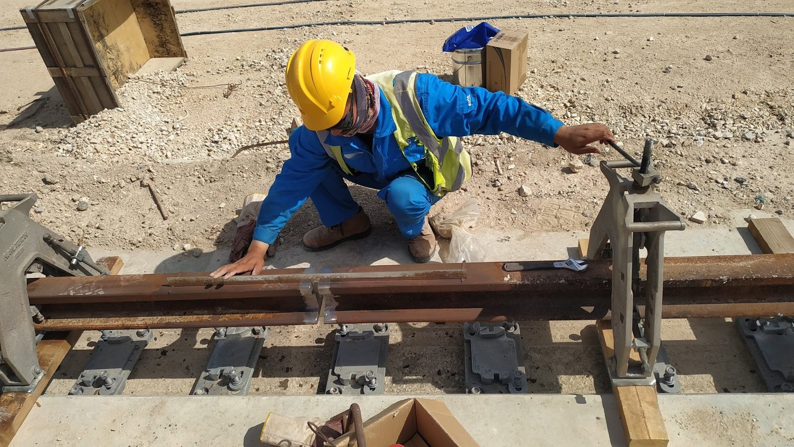 עובד בכובע קסדה מבצע עבודות ריתוך והתקנת מסילת רכבת באתר תשתית