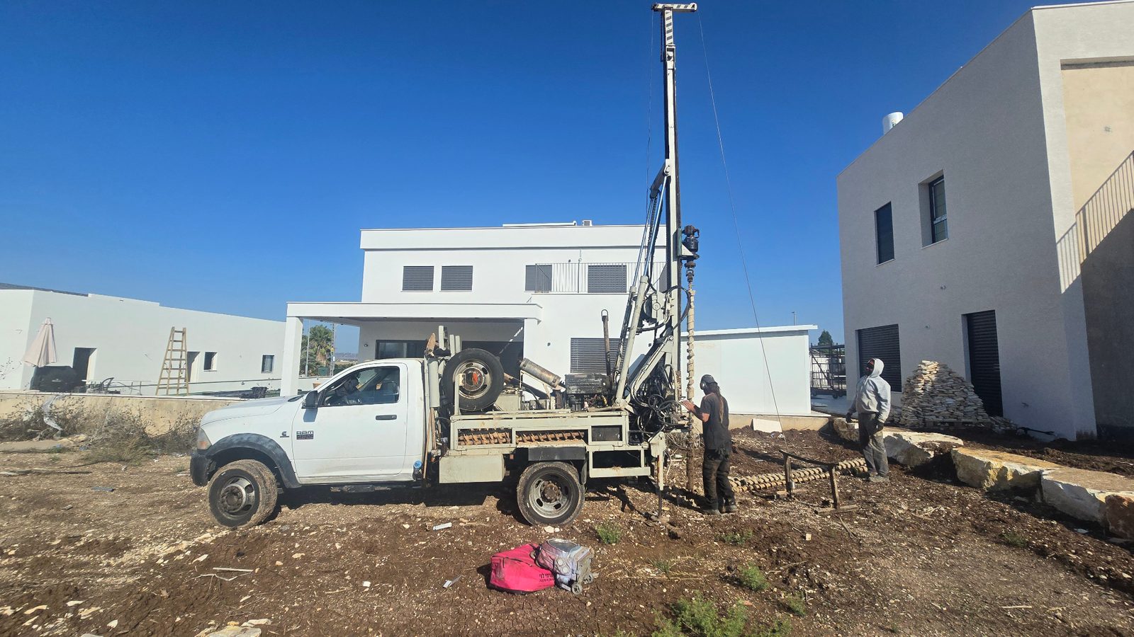 משאית קידוח מבצעת קידוחי ניסיון לבחינת קרקע בחצר בית מגורים